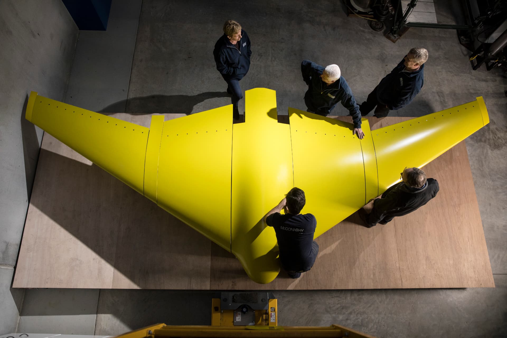 Overhead view of a large yellow composite wing structure being assembled by the McConaghy team