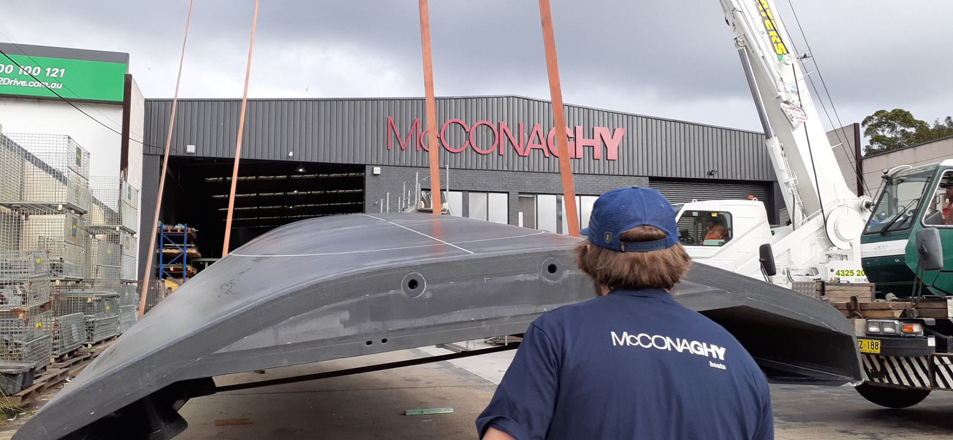 Carbon composite hull shell craned outside the McConaghy Australia build hall while a technician watches