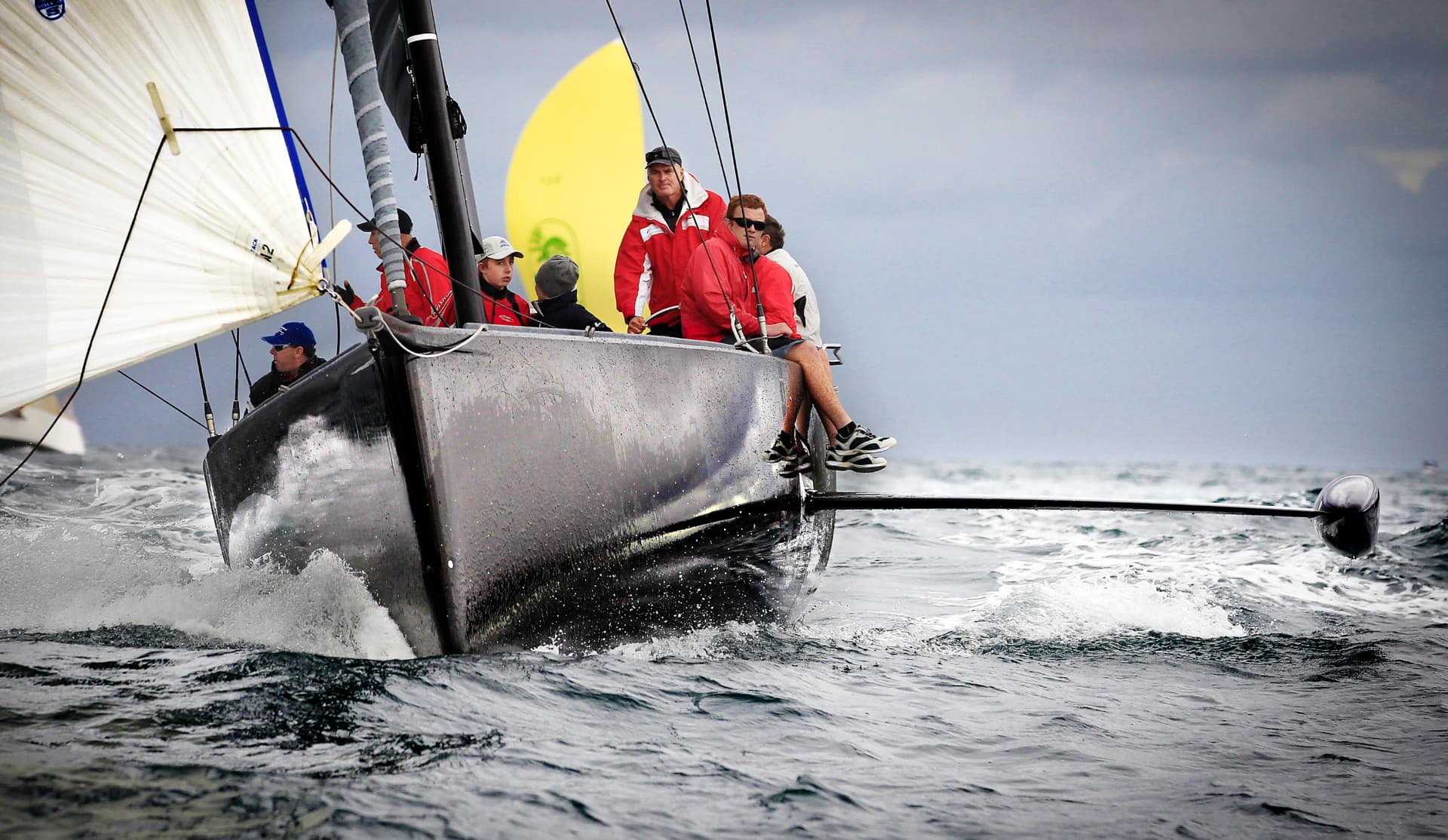 Crew hiking out on a McConaghy-built carbon racing yacht driving through open water