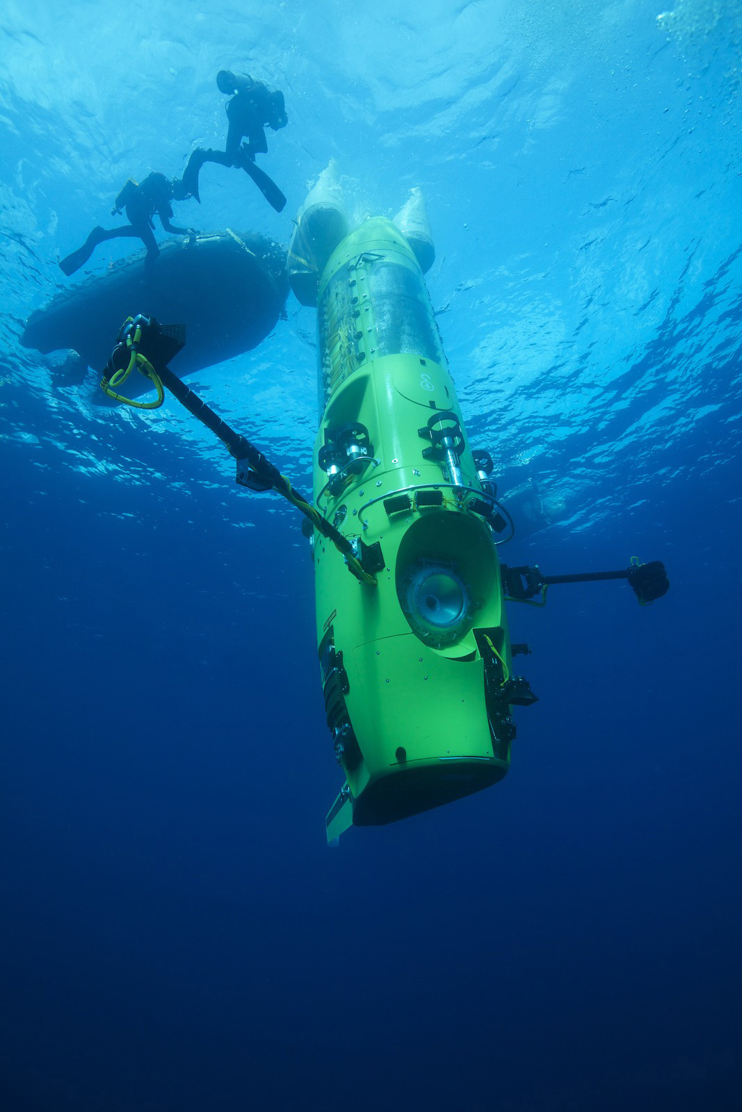 Deep-sea submersible with composite fairings descending below the surface alongside divers
